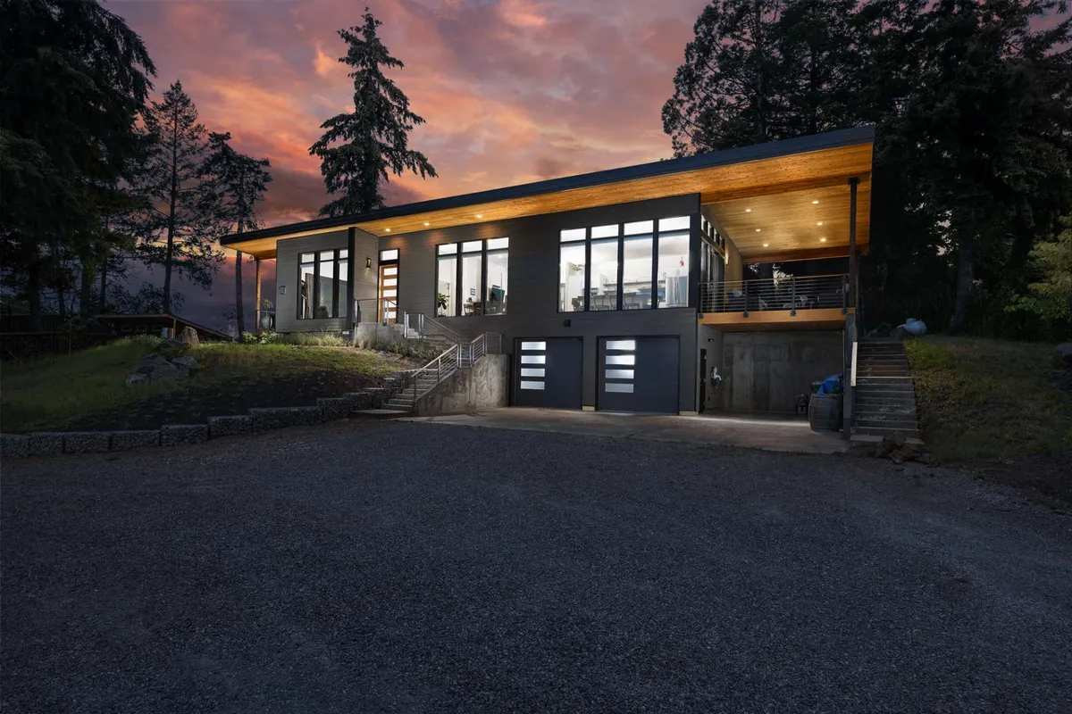 A striking exterior view of the villa showcasing its modern architecture, expansive windows, wooden overhang, and a welcoming stone pathway leading to the entry. The scene invites guests to imagine outdoor gatherings and the transition between indoor and outdoor living.