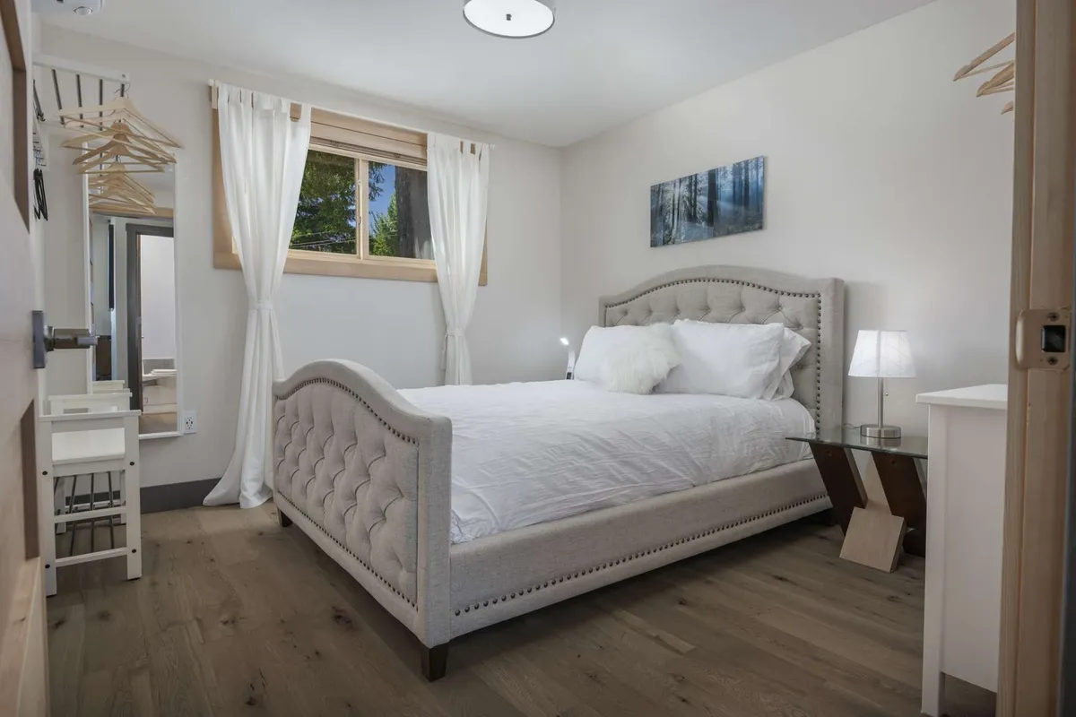 A peaceful bedroom scene with a bed, window letting in natural light, decorative painting, and a lamp. The light filtering through the window accentuates the cozy, welcoming environment.
