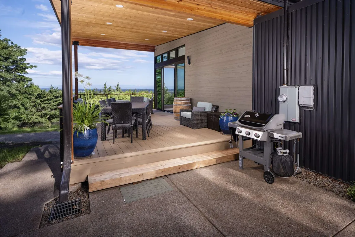 A stylish outdoor dining area with a table set for a meal, a grill nearby, and lush planters surrounding the space. The scene is bathed in warm evening light, suggesting sunset dinners and celebratory gatherings.