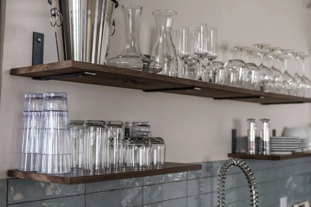 A sophisticated bar area with shelves of glassware, a silver bucket, and a modern sink, set up for preparing drinks or enjoying casual conversations. The space exudes an inviting, upscale mood, perfect for celebratory toasts, coffee breaks, or unwinding after a productive day.