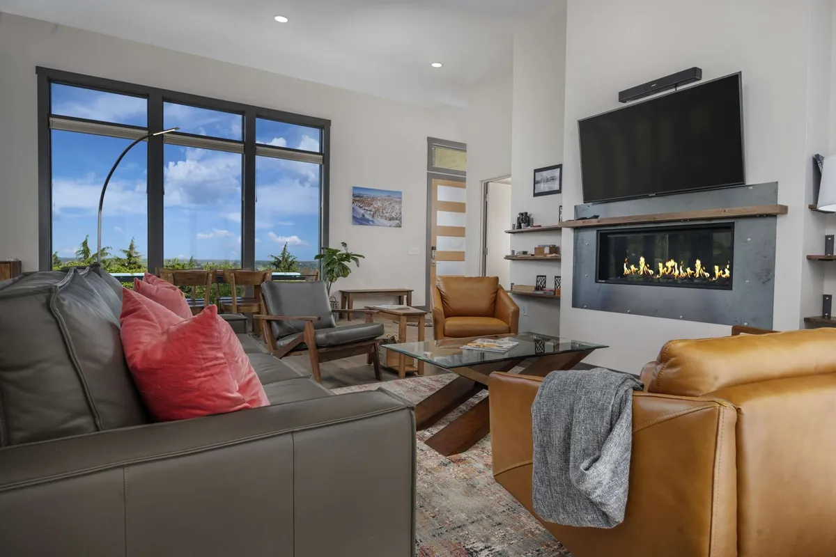 This image features a spacious and comfortable living area with large windows that flood the room with natural light, a modern fireplace for warmth and ambiance, cozy seating, and tasteful artwork. The layout is ideal for both relaxing and entertaining, making it a perfect representation of one of the villa's communal living spaces.